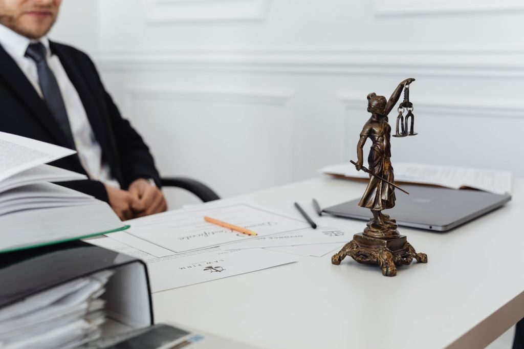 Patrimonial e Inmobiliario A legal professionals workspace featuring Lady Justice statue, documents, and a laptop.